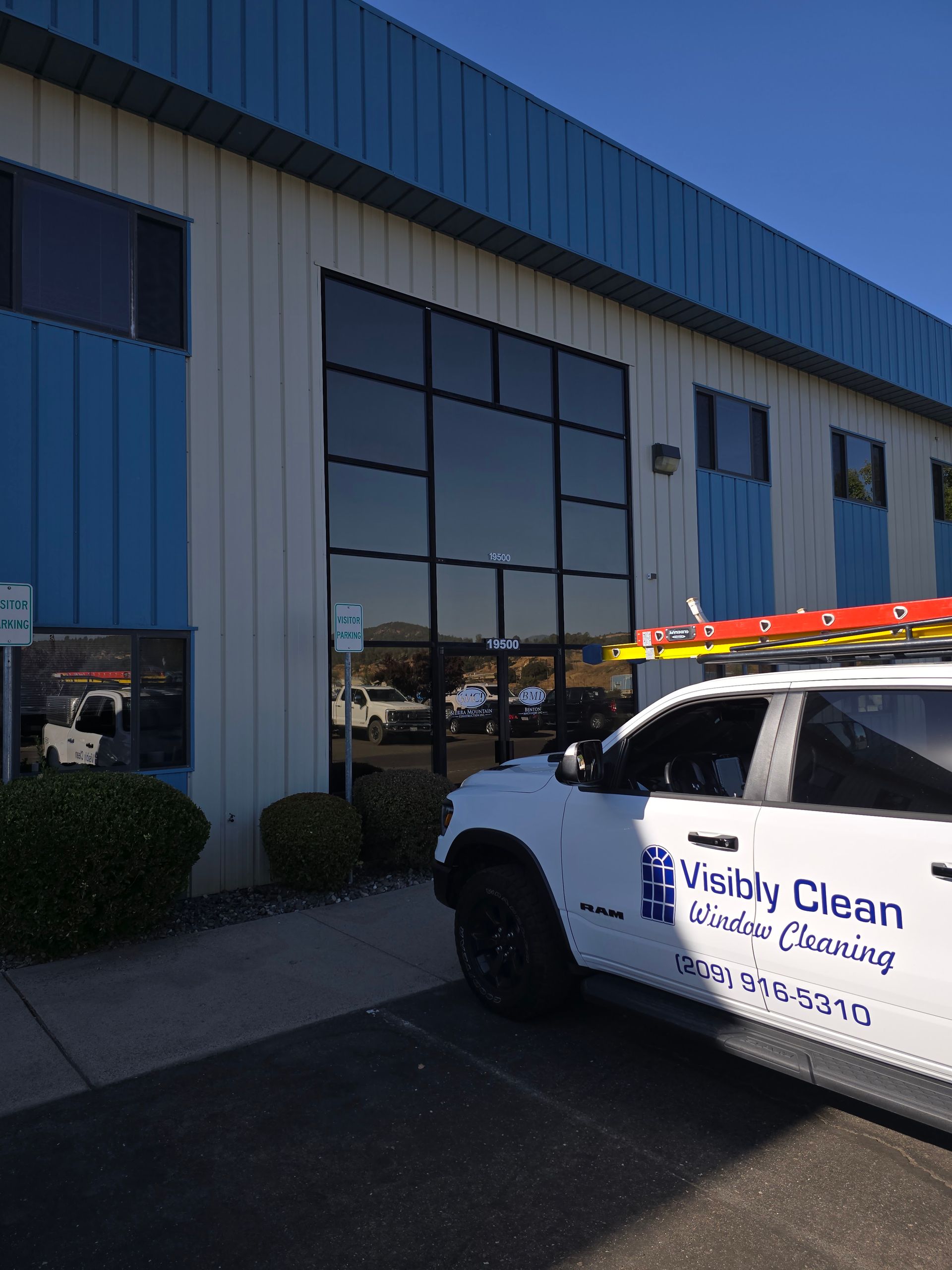 A white van with a ladder on top of it is parked in front of a building.
