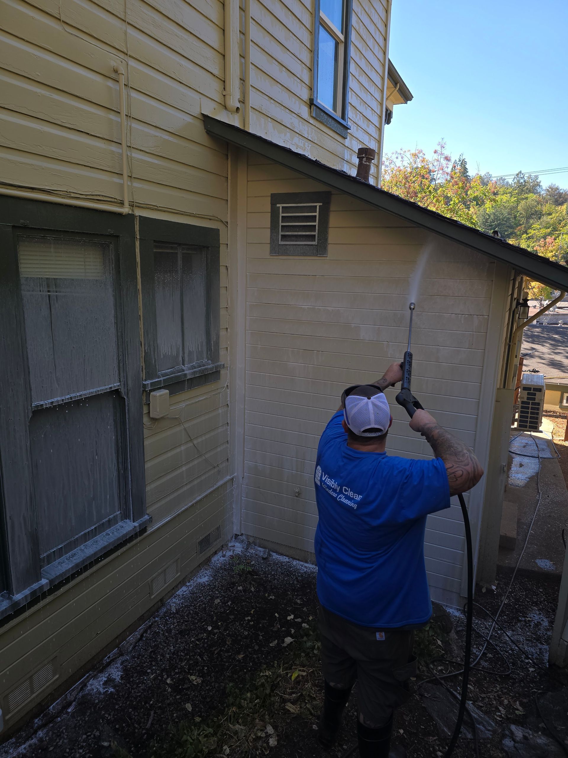 A man in a blue shirt is cleaning the side of a house