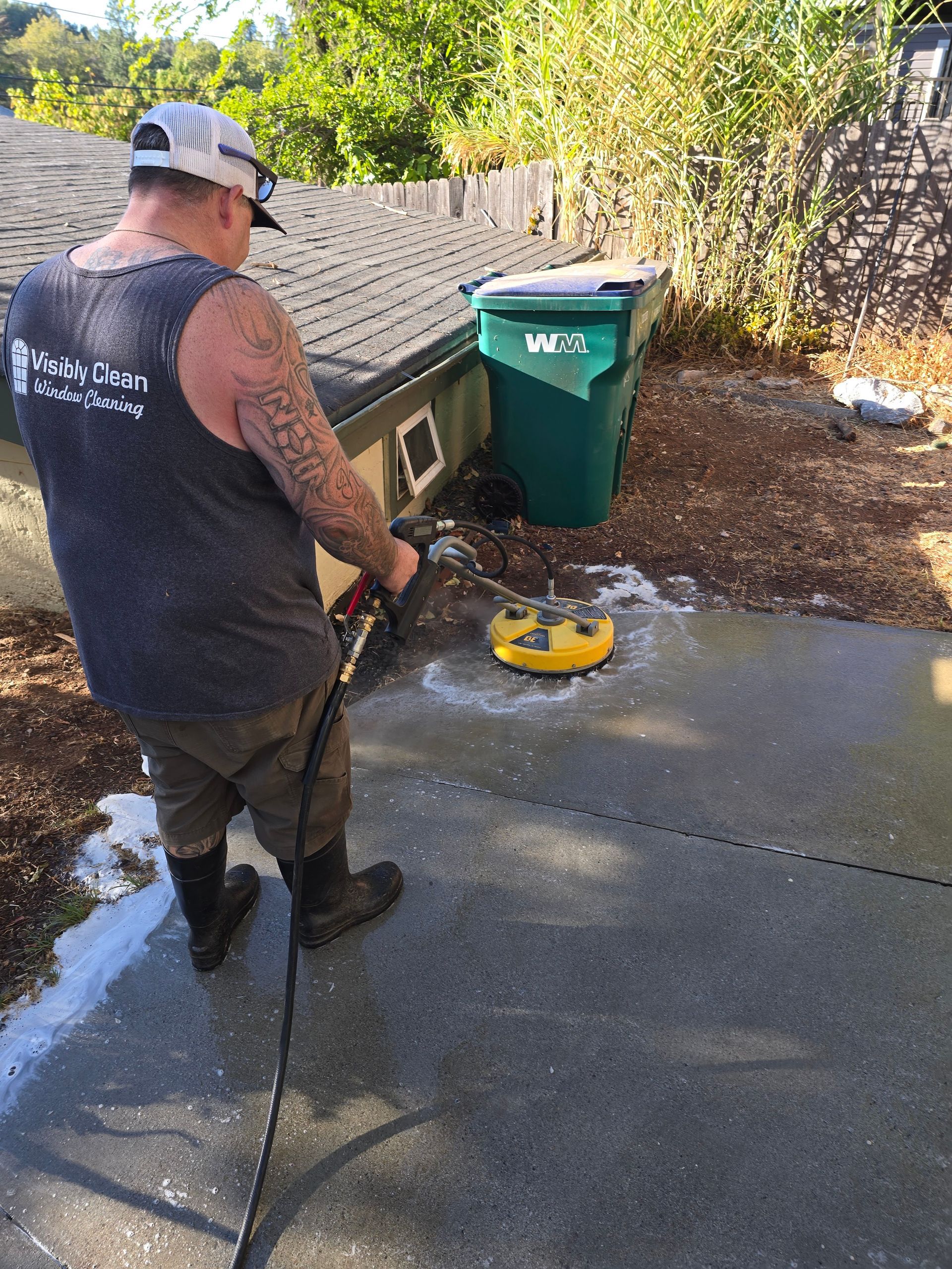 A man is using a high pressure washer to clean a sidewalk.