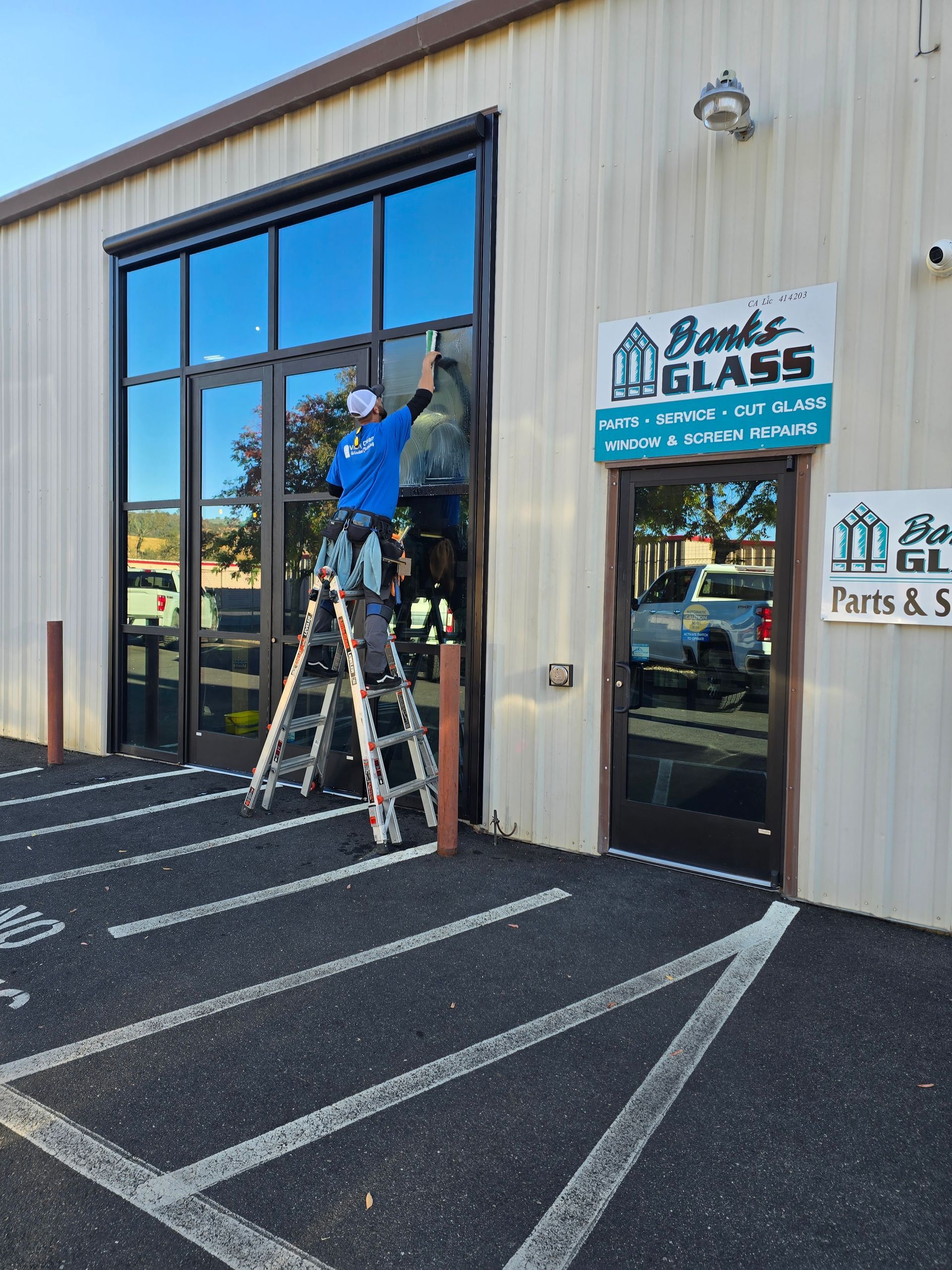 A man on a ladder is cleaning a window in front of a store called brooks glass