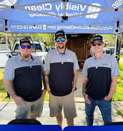 Three men are posing for a picture in front of a blue tent that says nssu