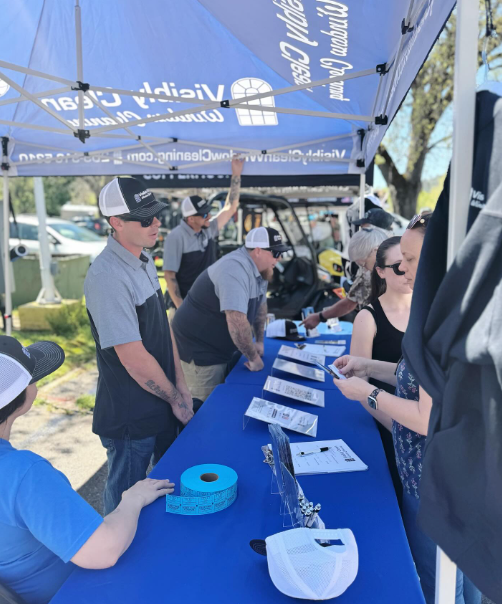 A group of people standing around a table under an umbrella that says ' new ' on it