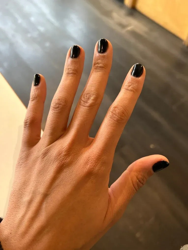 Manicurist painting a client's fingernails red at a salon, with nail polish bottles and candles in the background.