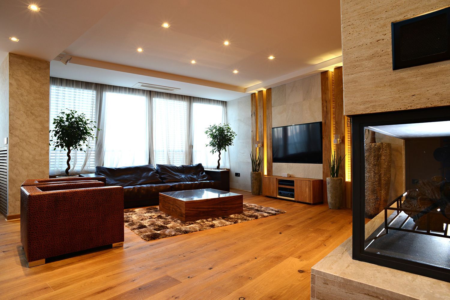Modern living room with leather furniture, hardwood floors, fireplace, and large windows. Modern living room with leather furniture, hardwood floors, fireplace, and large windows.