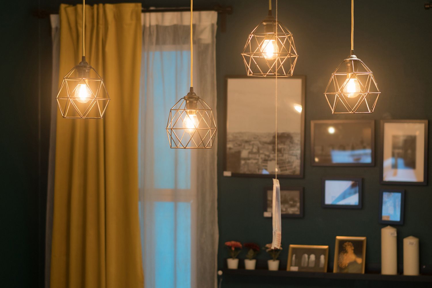 Geometric pendant lights illuminating a room with dark teal walls, framed artwork, and yellow curtains. Geometric pendant lights illuminating a room with dark teal walls, framed artwork, and yellow curtains.