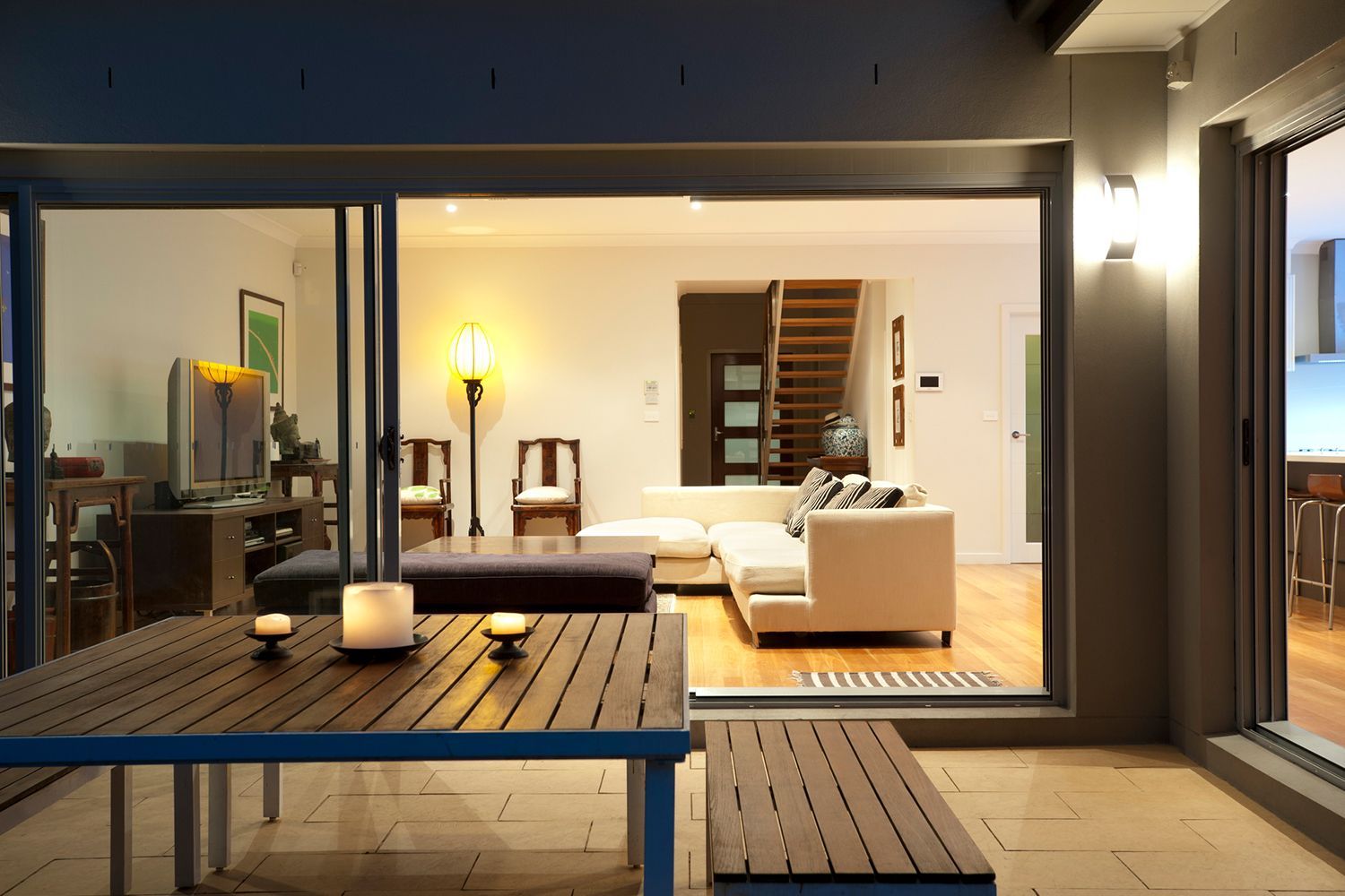 Outdoor patio with a wooden table, overlooking a living room with white furniture and stairs. Outdoor patio with a wooden table, overlooking a living room with white furniture and stairs.