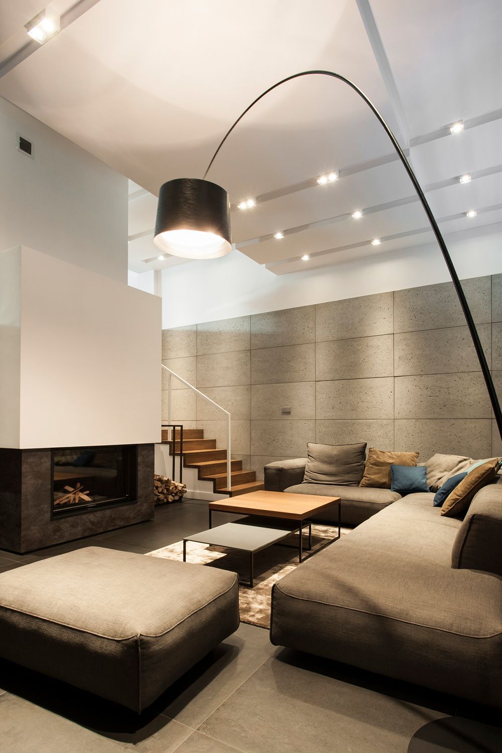 Modern living room with fireplace, stairs, concrete wall, sofa, and arc lamp. Modern living room with fireplace, stairs, concrete wall, sofa, and arc lamp.