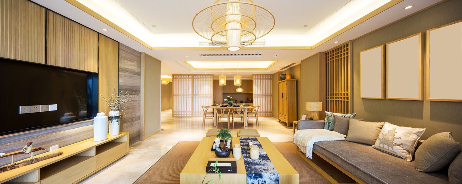 Living room with a sofa, coffee table, TV, and dining area in the background. Beige and gold color scheme.