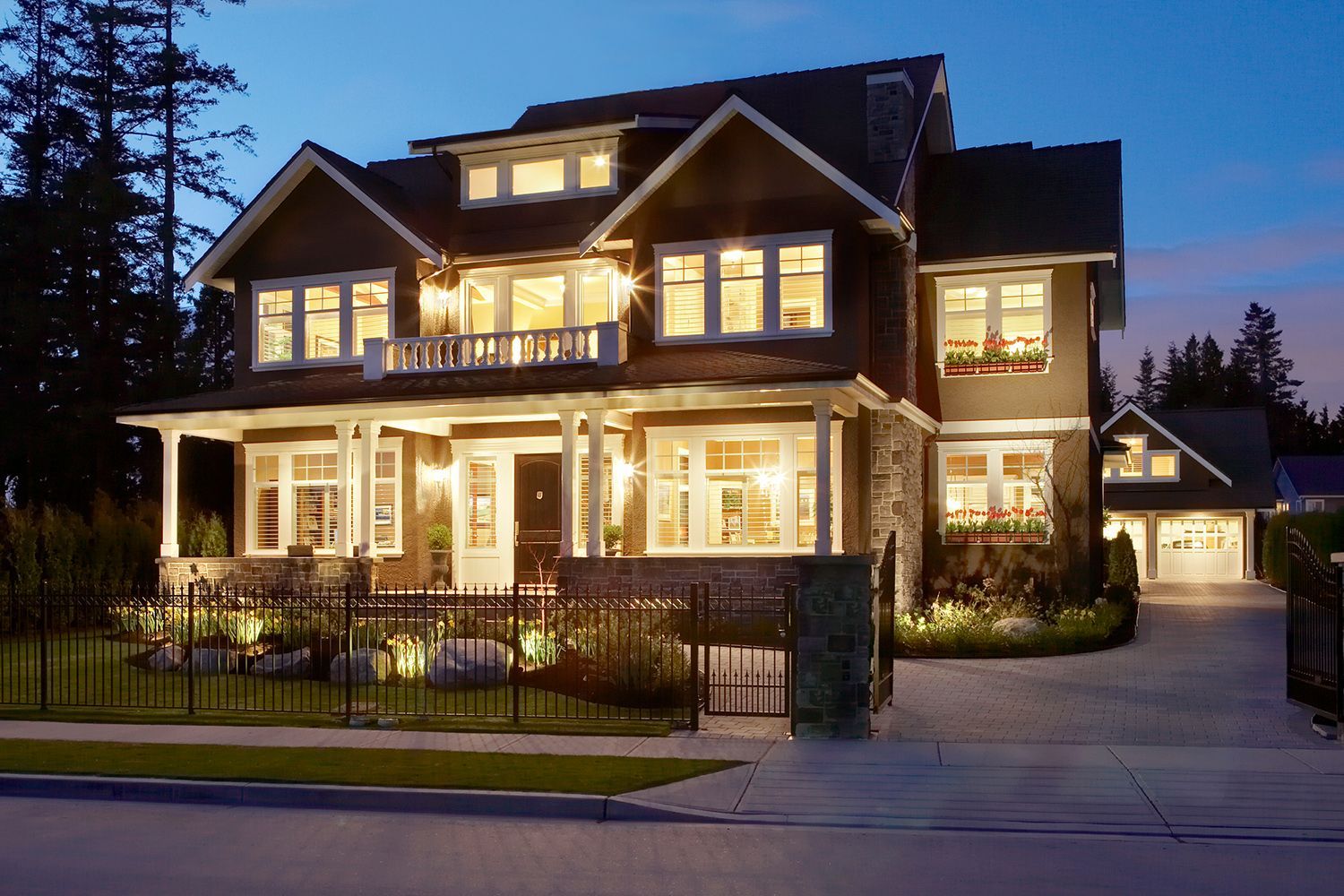 Brown and beige Craftsman-style house at dusk, lit interior, stone and wood exterior, with a front porch, and a driveway. Brown and beige Craftsman-style house at dusk, lit interior, stone and wood exterior, with a front porch, and a driveway.