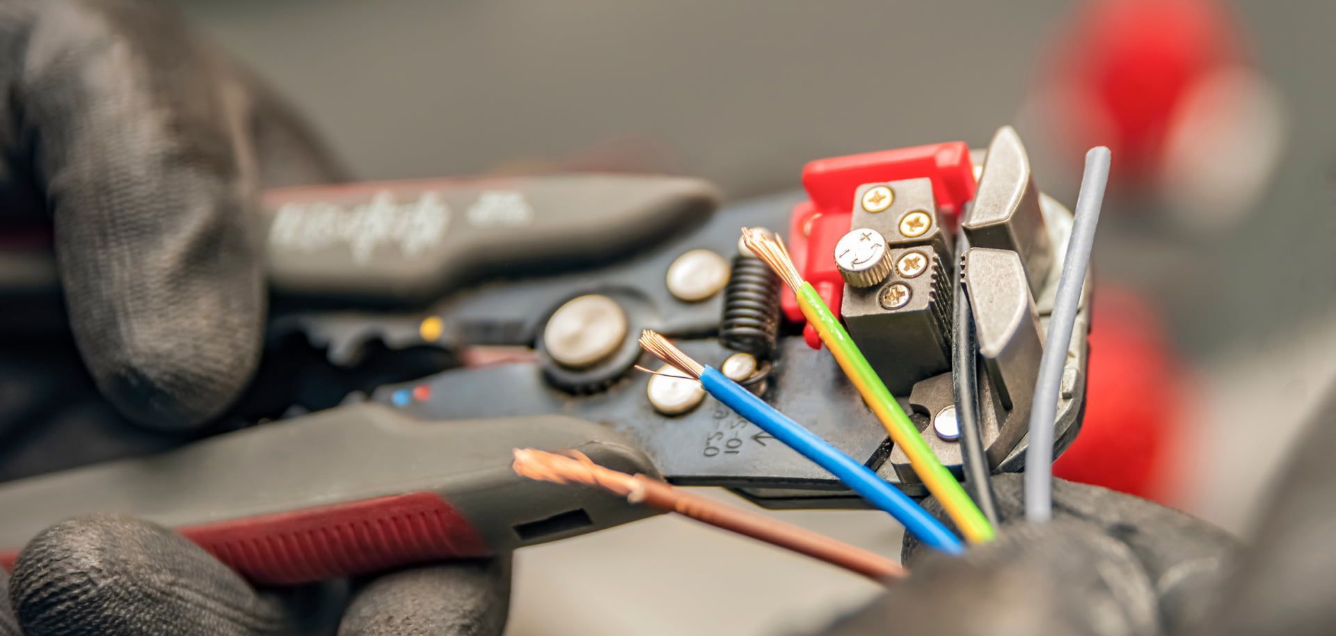 Close-up of a person with gloved hands using wire strippers on electrical wires.