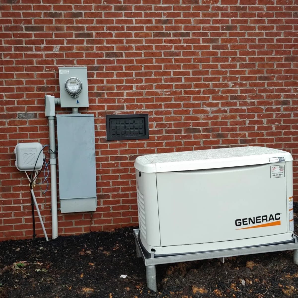 A white Generac generator on a metal stand next to a brick wall with electrical components.