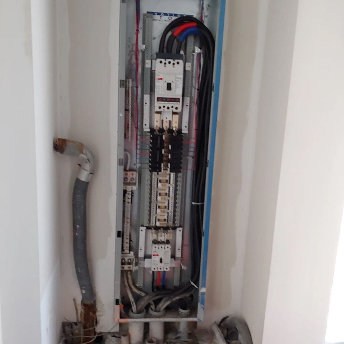 Open electrical panel with wires and circuit breakers installed inside a white wall.