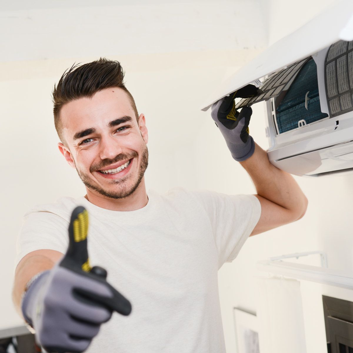 Man wearing gloves cleaning an air conditioner filter and giving a thumbs-up.