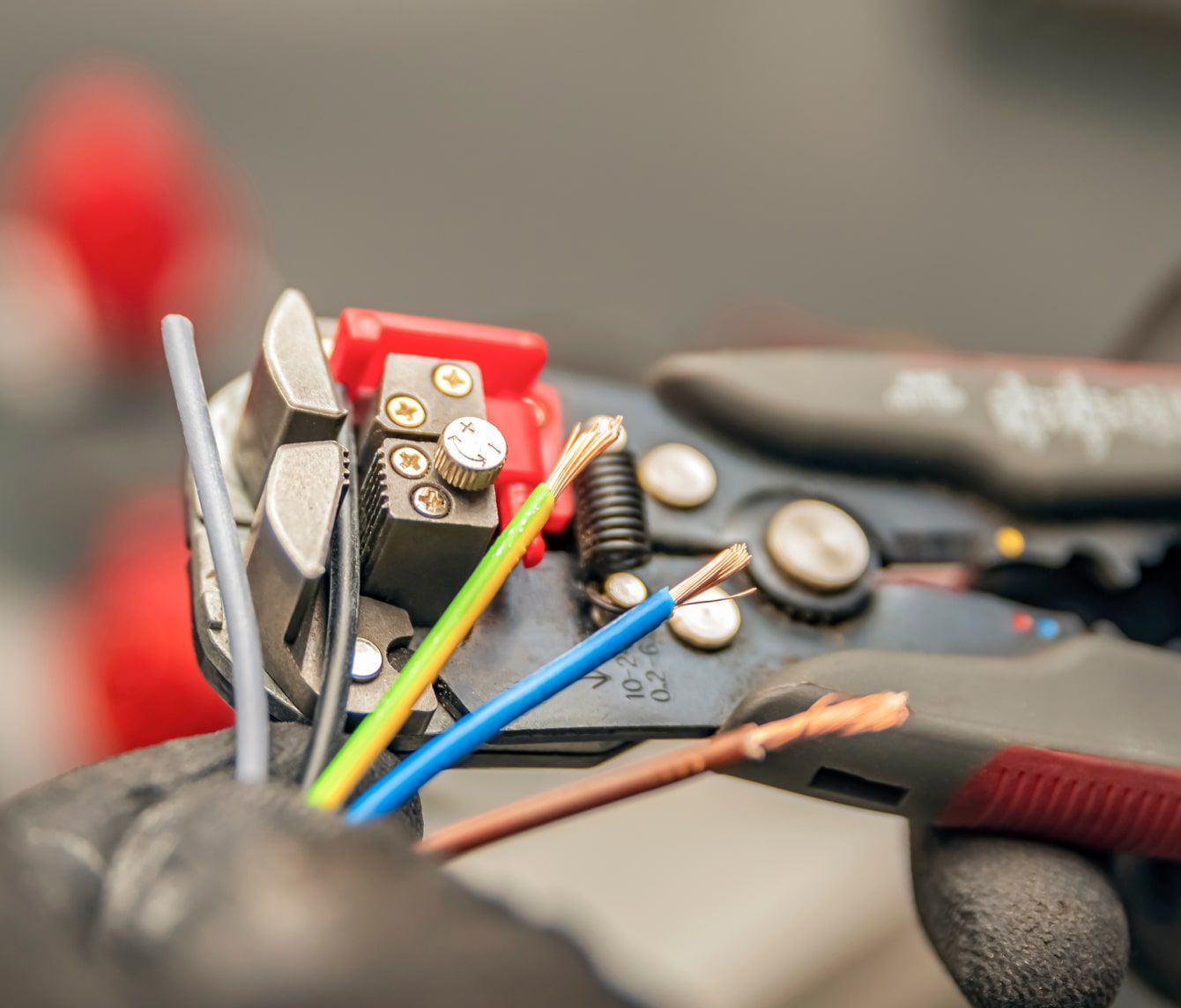 Electrician using wire stripper to expose the copper wires of electrical cables. Close-up with focus on tools and colorful wires.