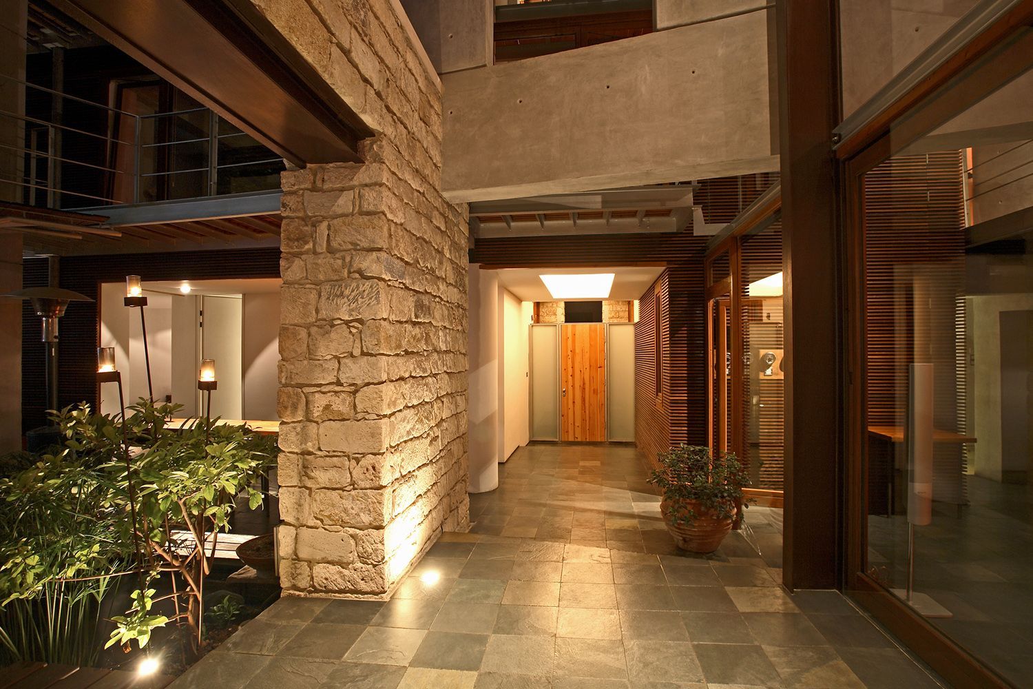 Entryway of modern building with stone wall, wooden accents, and indoor plants, lit at night. Entryway of modern building with stone wall, wooden accents, and indoor plants, lit at night.