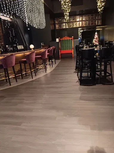 Bar with burgundy stools, dark wood floors, and decorative lights. A red throne is in the background.