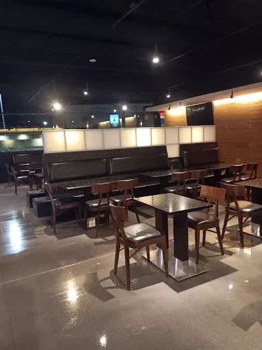 Restaurant interior with tables, chairs, and a long booth. Dark wood and black seating.