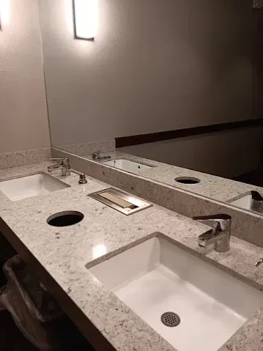 Two sinks, mirror, and countertop in a restroom. Granite countertop, two sinks, and a recessed soap dispenser.