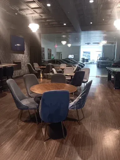 Interior of a lounge with a round table and chairs.  Pool table visible.  Wood flooring, dark walls, and bright lighting.
