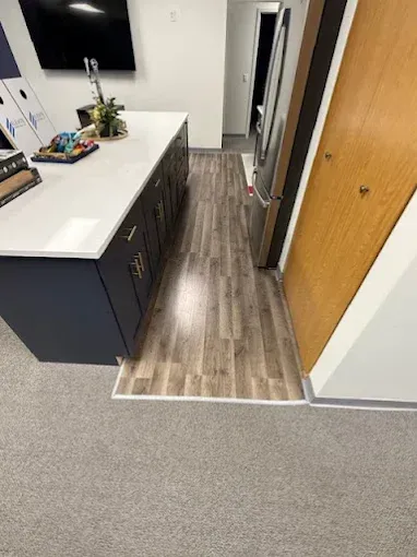 Kitchen with blue island, wood-look floor, and light gray carpet. Door on right.
