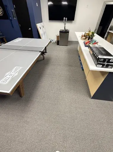 A recreation room with a ping pong table, bar, and TV; gray carpeted floor.