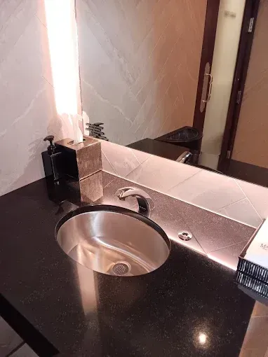 Bathroom sink with a black countertop, mirror, and a gold tissue box.