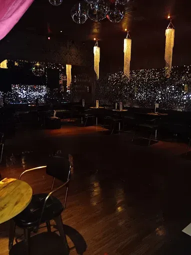 Dark nightclub interior, wooden floors, tables, chairs, disco balls, and hanging lights.