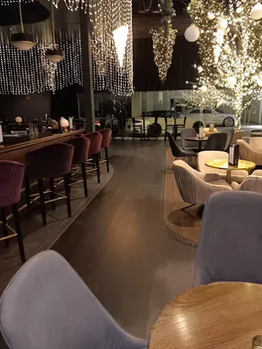 Interior of a bar with seating, dimly lit. Velvet bar stools, tables, and a tree with lights create a warm ambiance.