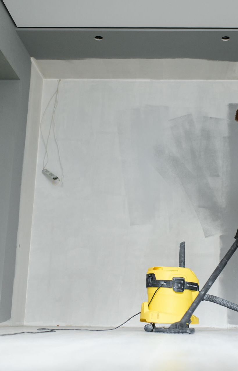 Yellow vacuum cleaner in a room under construction, grey walls and ceiling.