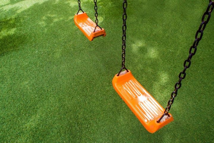Two orange swings hanging from chains against a green grassy background.