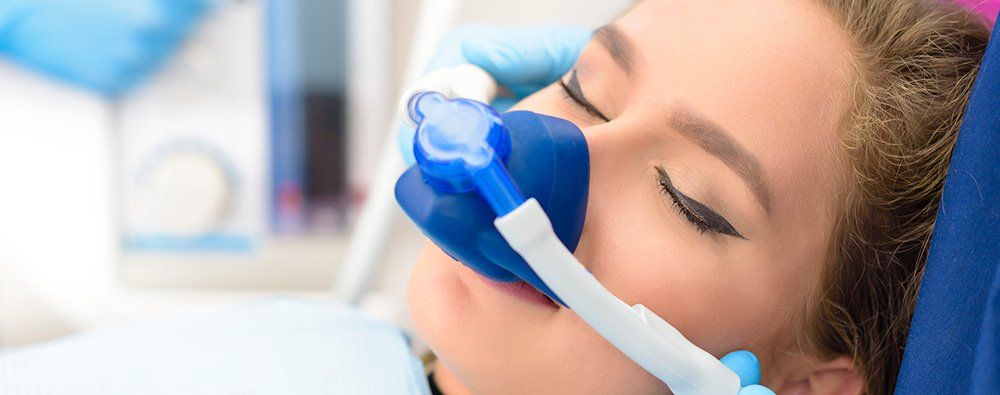 A woman is laying in a dental chair with an oxygen mask on her face.