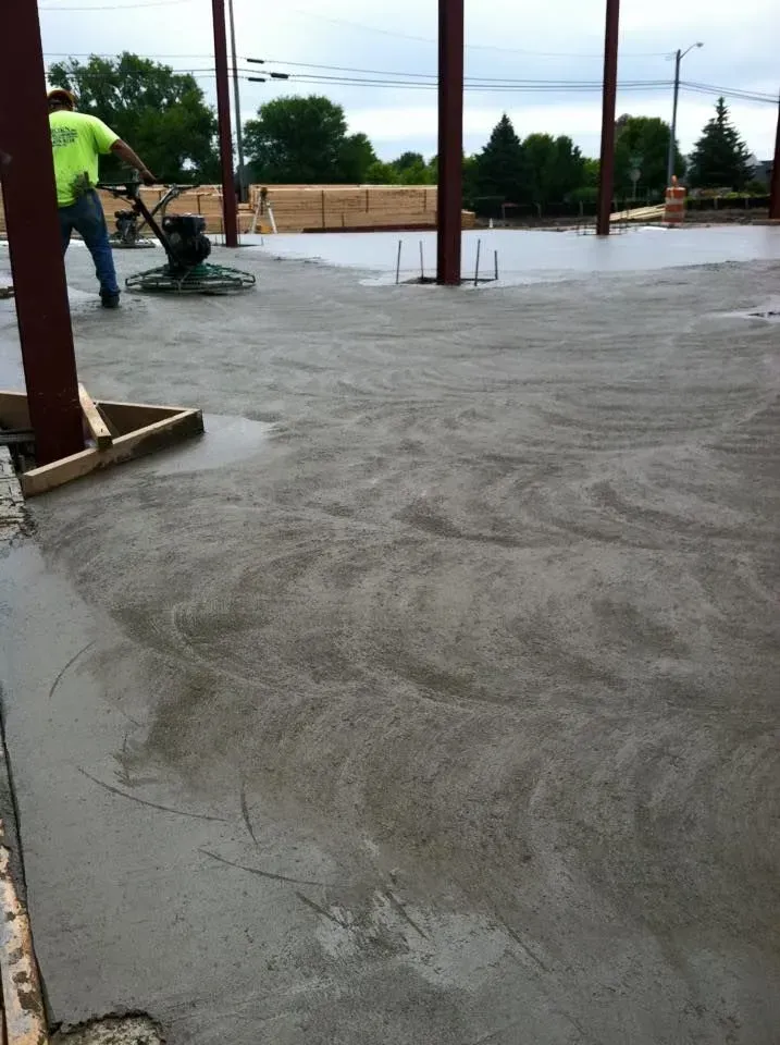 Worker smoothing wet concrete floor with a power trowel at a construction site.