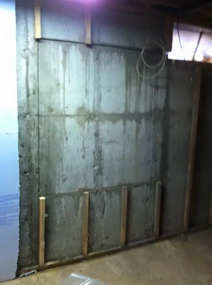 Concrete basement wall with wooden studs; unfinished, with wiring.