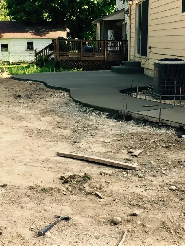 Concrete patio under construction next to a house and wooden deck.