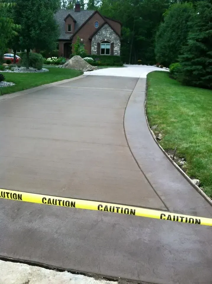 Newly poured concrete driveway with caution tape in front of a house.