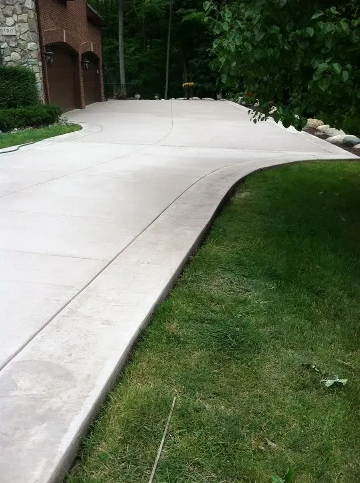 Concrete driveway curving beside a grassy lawn, leading to a brick house with garage doors.