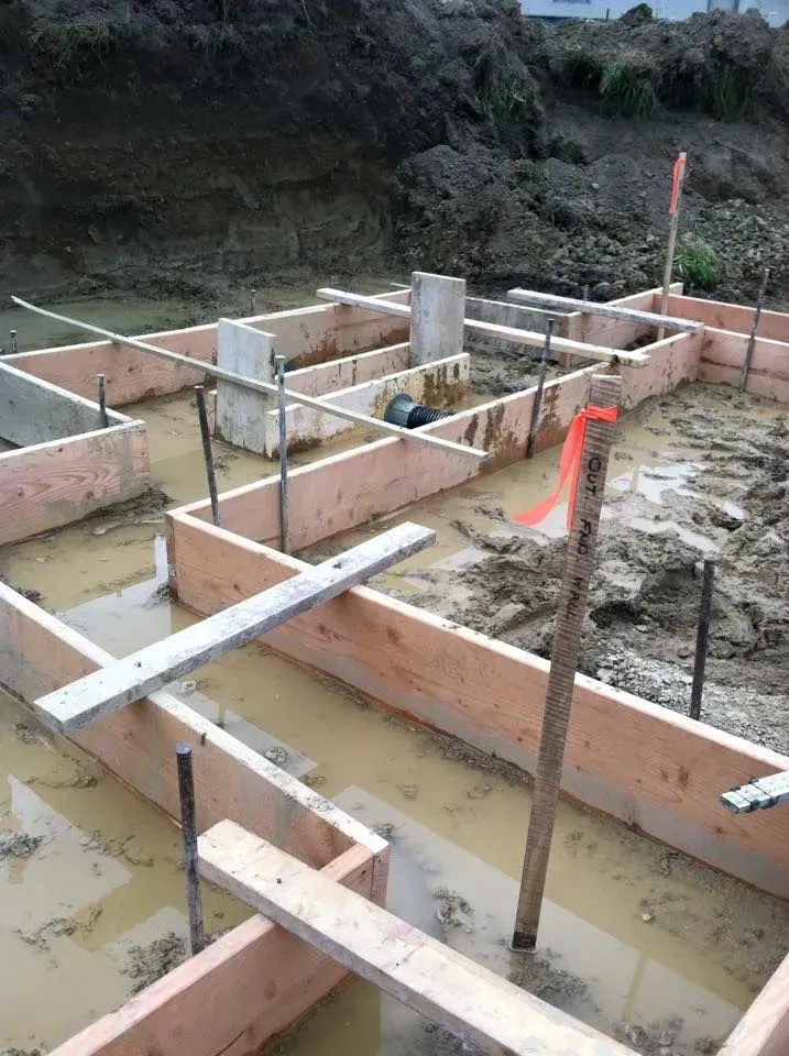 Foundation forms with wet soil, wooden frames and rebar, outdoors.