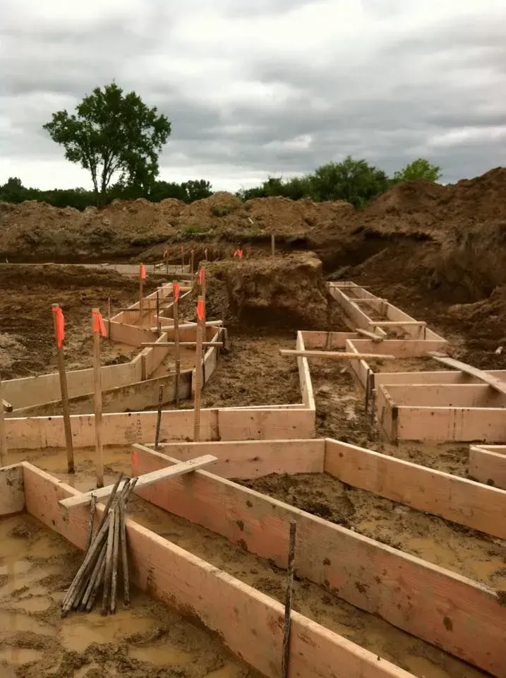 Wooden forms for a building foundation under construction in muddy soil, with orange marker flags.