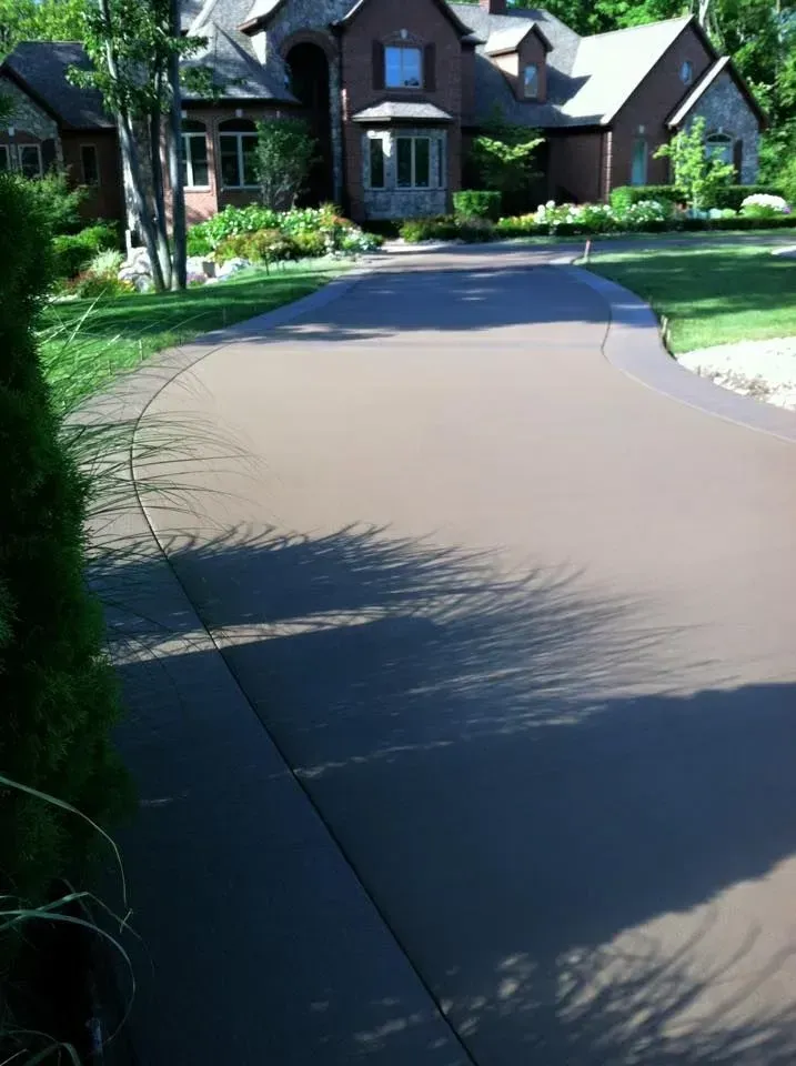 Long, curving driveway leads to a large, brown house with lush green lawn.