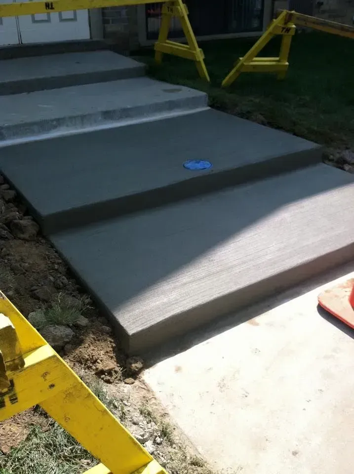 Newly poured concrete steps, gray, leading up from a sidewalk. Yellow safety barriers are present.