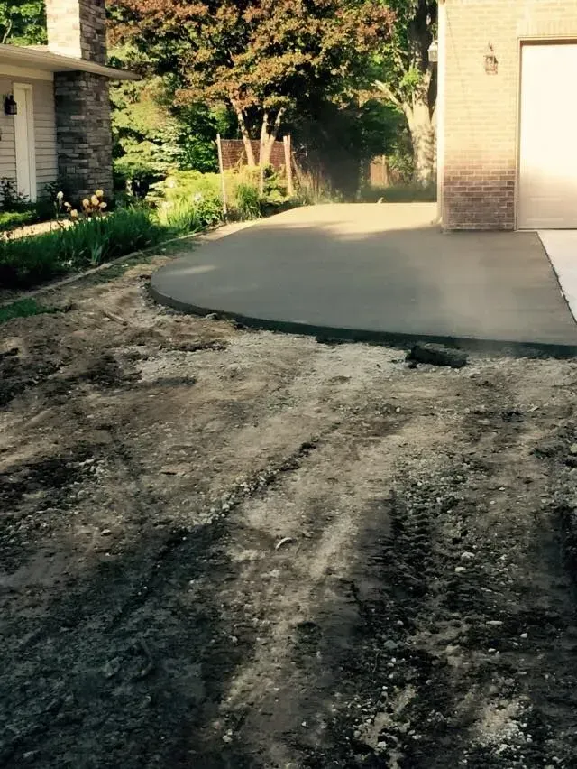 Newly poured concrete driveway with exposed dirt in front, near a house.