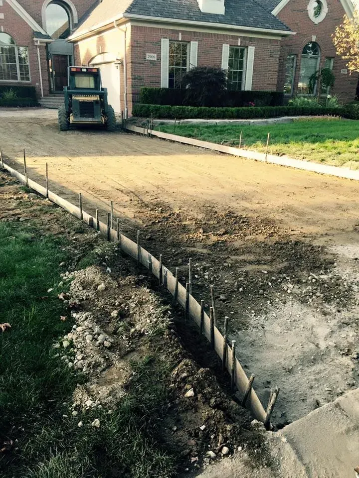 Driveway construction at a house with a concrete border, a small tractor, and freshly dug earth.
