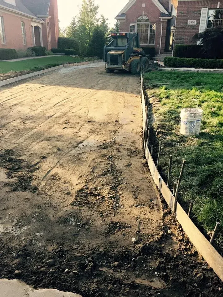 Construction site: dirt road with concrete forms alongside grass, front-end loader in the distance.