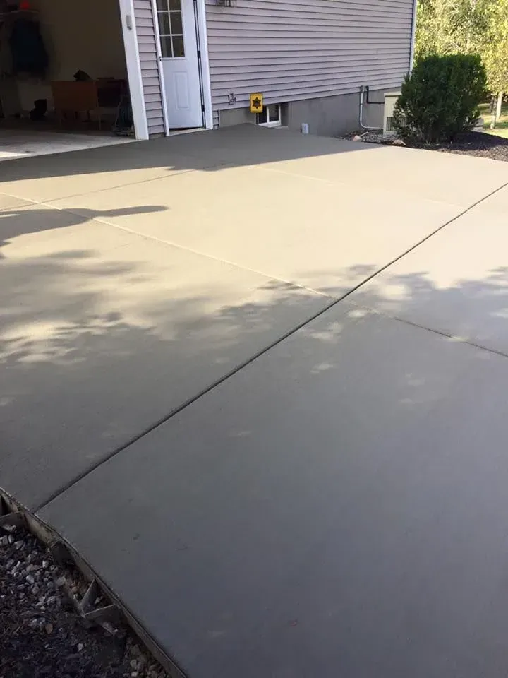 Newly poured concrete driveway next to a house with a white door and garage.