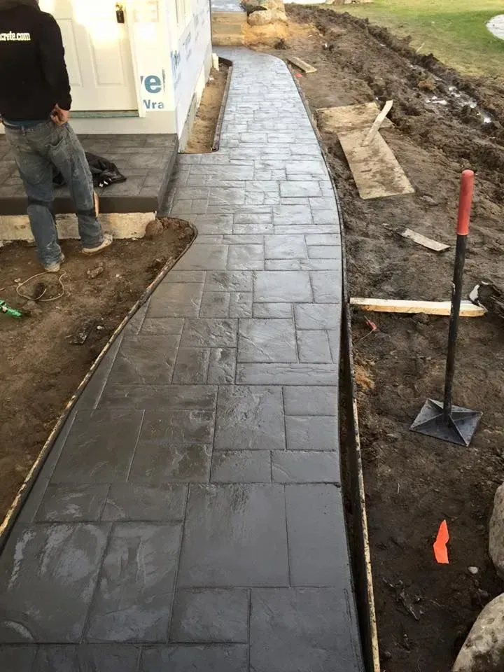Dark gray stamped concrete walkway being constructed near a building. A person stands nearby.
