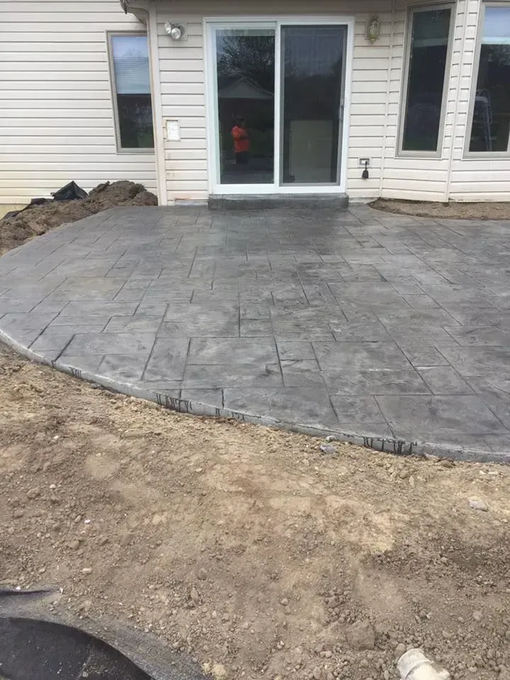 Gray stamped concrete patio outside a house with a sliding glass door.