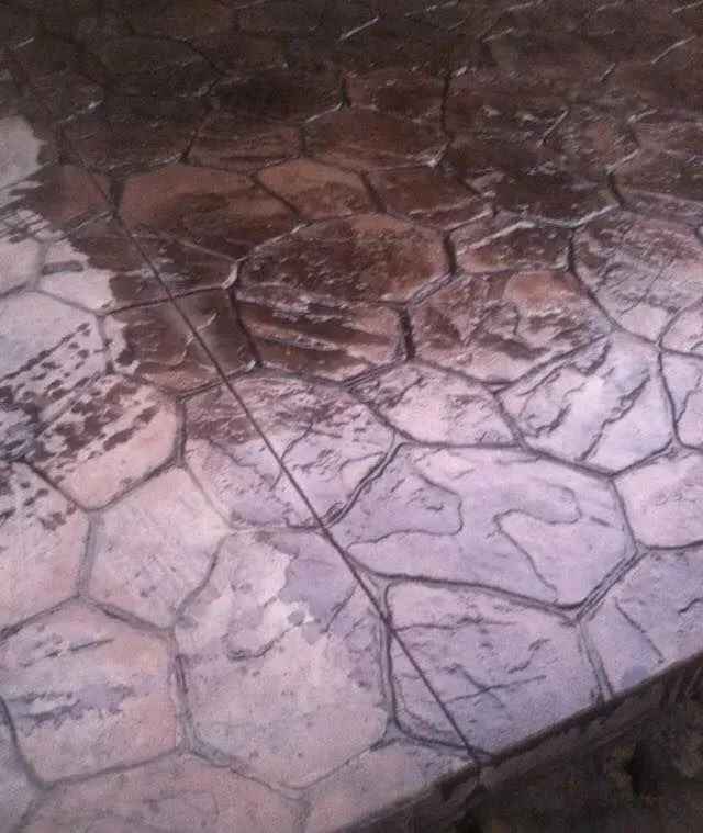 Stamped concrete patio, stone pattern, wet surface reflecting light, brown and gray tones.