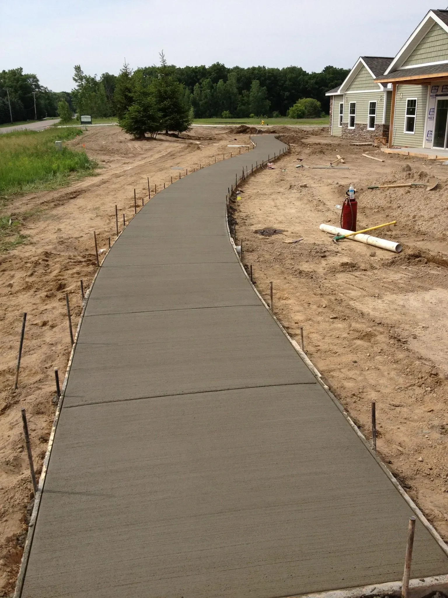 Freshly poured concrete sidewalk, curving through a construction site, flanked by dirt.