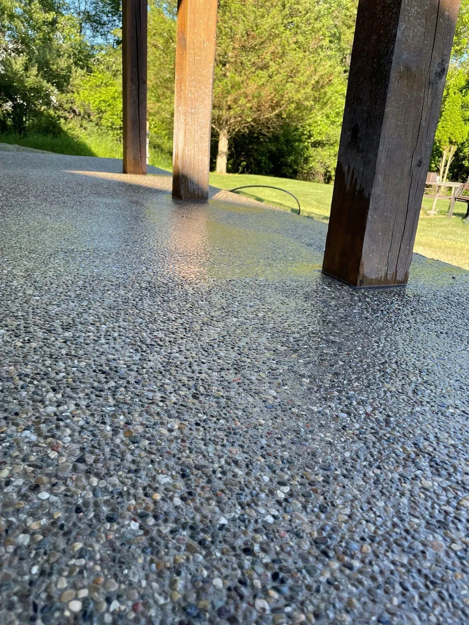 Exposed aggregate concrete patio with square support columns. Green trees in the background.