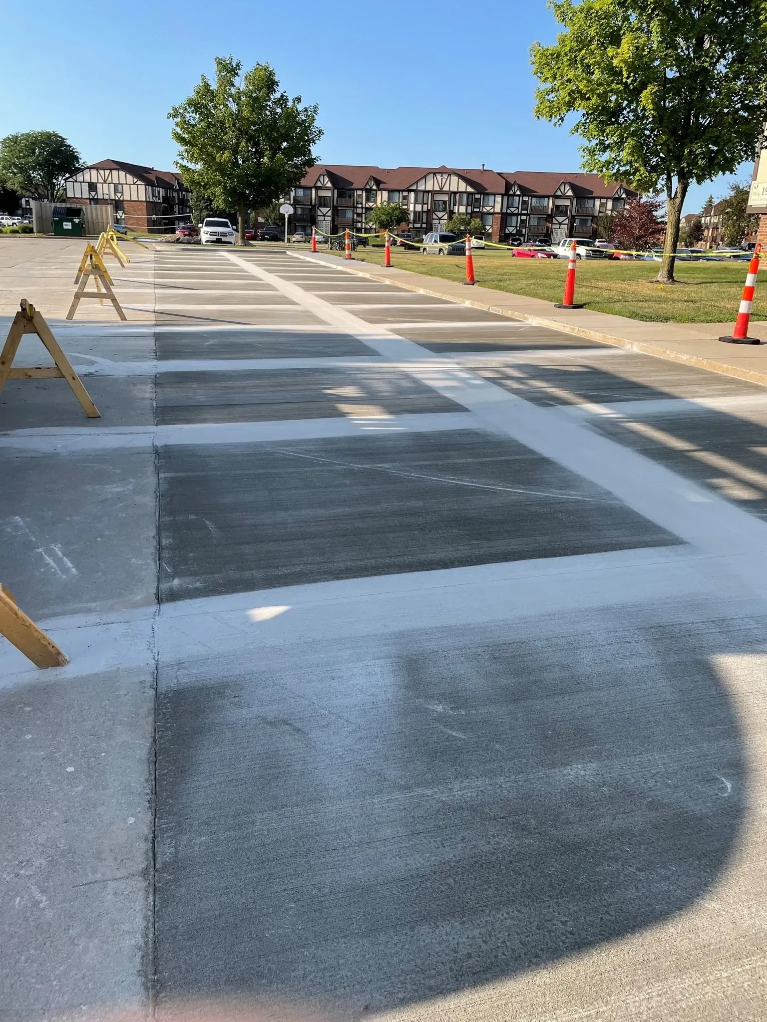 Parking lot undergoing resurfacing; sections painted gray with white lines. Wooden sawhorses and orange cones.